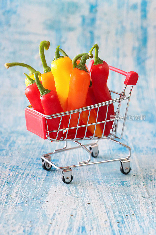 一组红、黄、橙迷你辣椒(Capsicum annuum)的微缩特写图像，模型购物车，健康食品店，斑驳的蓝色背景，重点放在前景，健康饮食理念